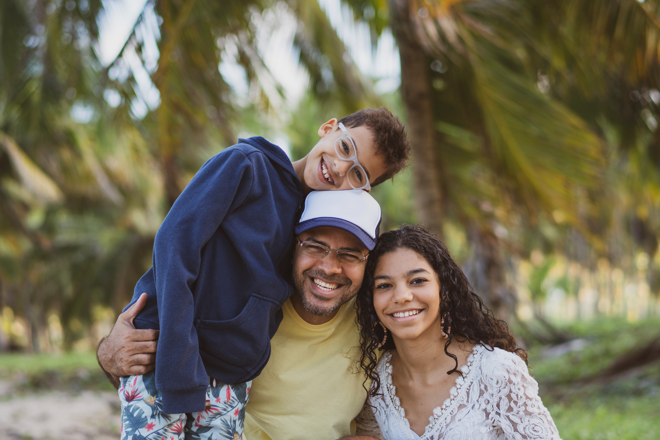 A young person is held up by their dad, with mom standing next to them. They smile happily at the camera. 