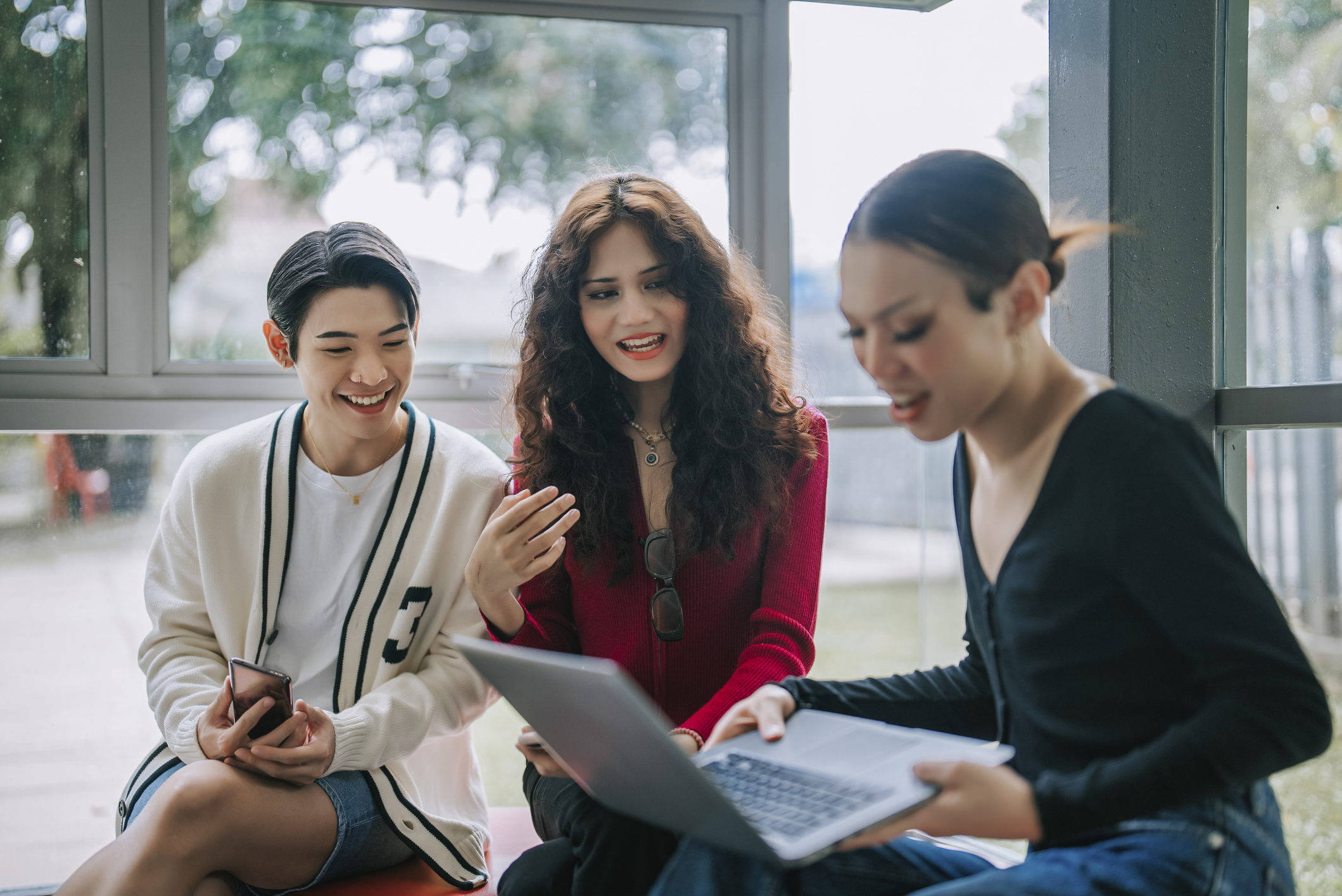 Three young Asian people discuss while looking at a laptop. 